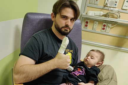 Ryan, Ellia's dad, holding her as a baby in exam room and giving thumbs up