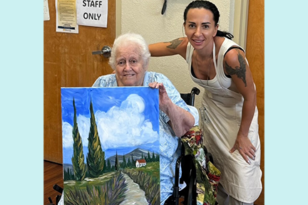 Tatiana, volunteer art teacher, and resident at Memorial Manor showcasing painting